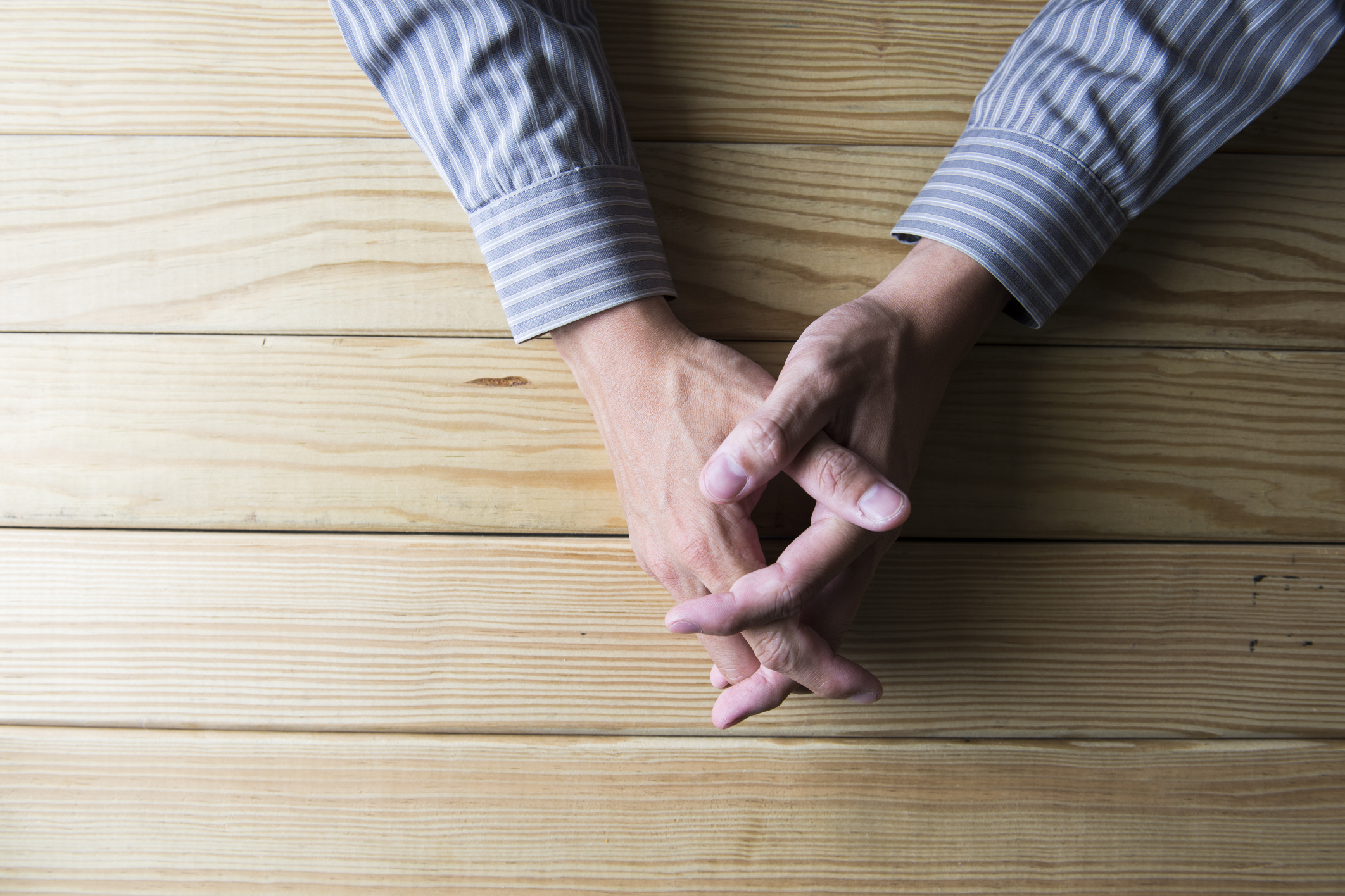 Close up on male hands folded in prayer at a wooden table