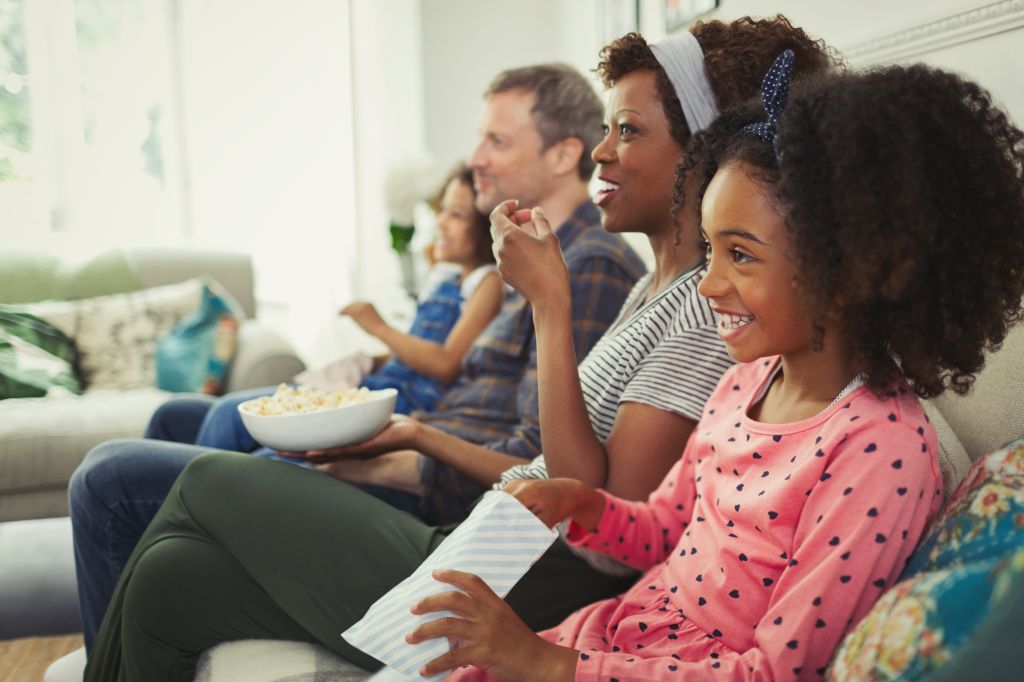 Young multi-ethnic family watching movie and eating popcorn on sofa