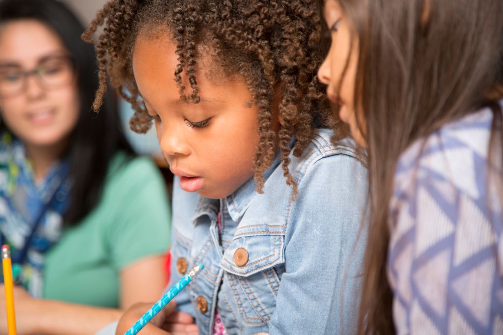 Teacher, mentor helps elementary-age schoolgirls with homework.