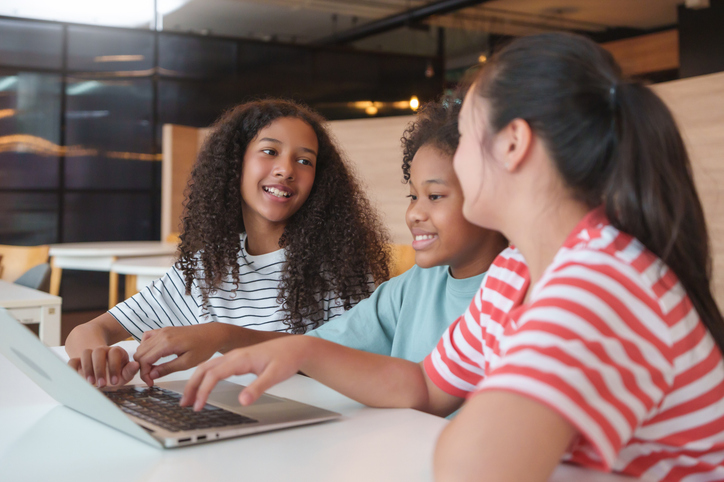 Smiling Three Diverse little girls learning together on a laptop in a classroom, showing joy, Multiethnic children with E-learning and online classroom in a relaxed educational.